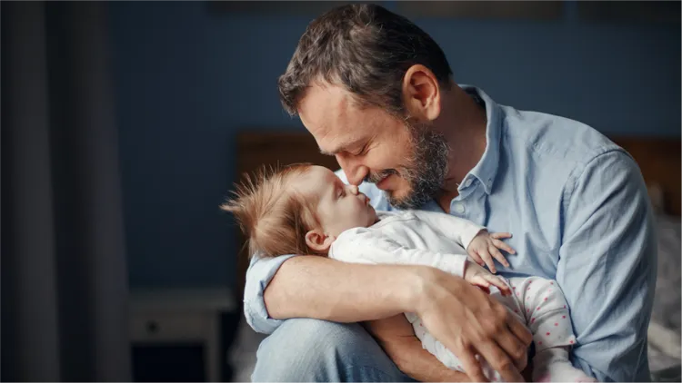 An adult man gently cradles a small baby in his arms.