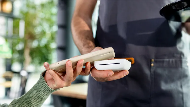 A customer holds a smartphone over a wireless card reader to complete a contactless payment.